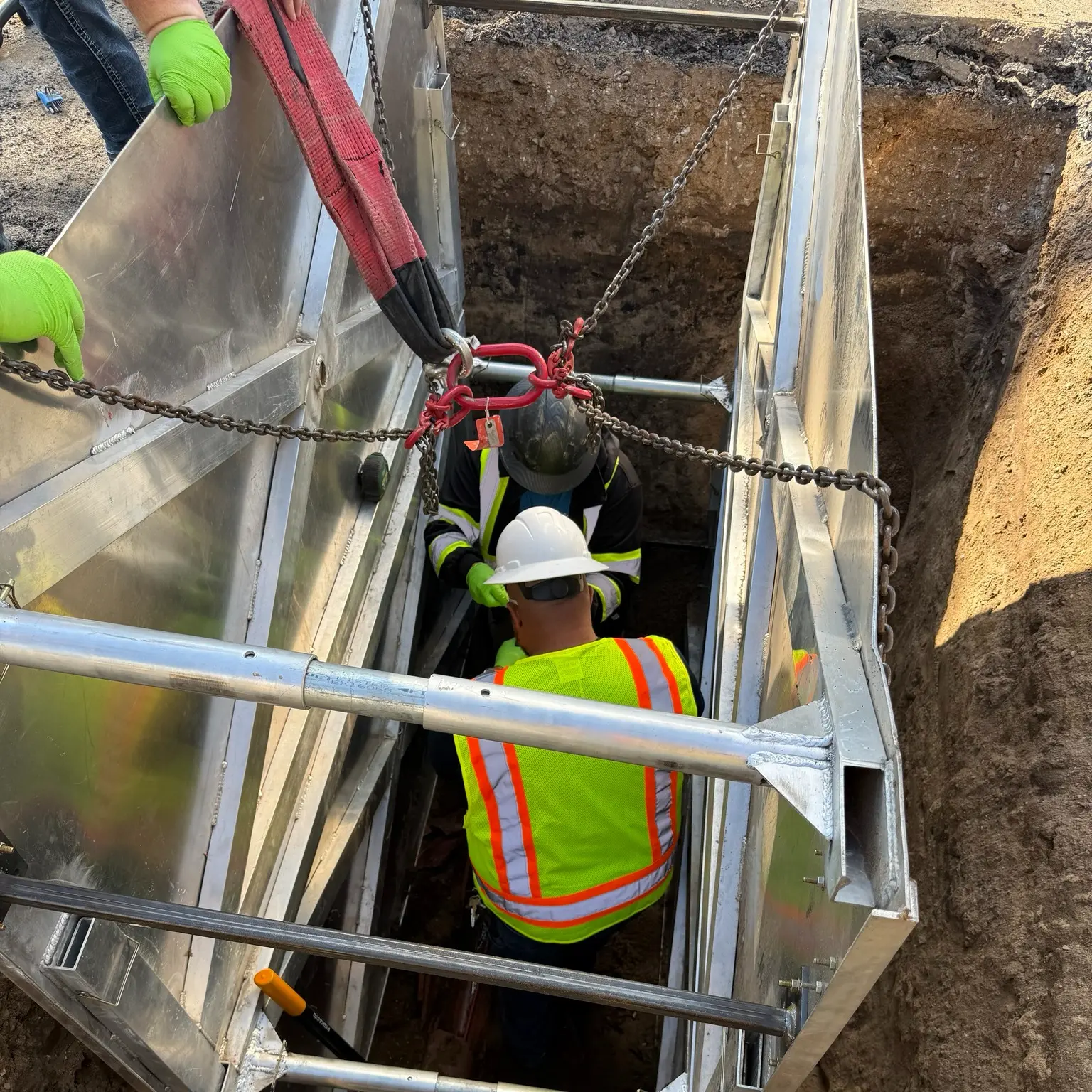 Workers in safety gear using a trench box for deep sewer line replacement, emphasizing excavation safety and teamwork.