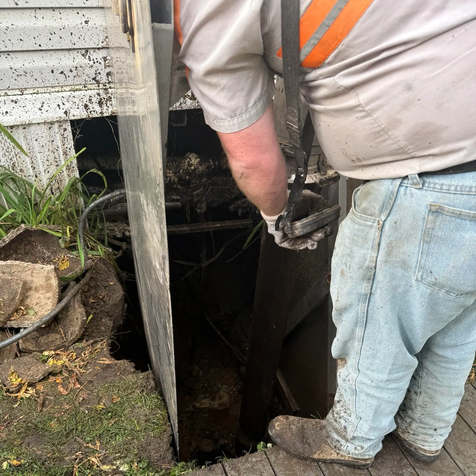 Plumber performing maintenance on a complex water system, addressing drainage issues near a sewer access point, showcasing expertise in plumbing solutions.